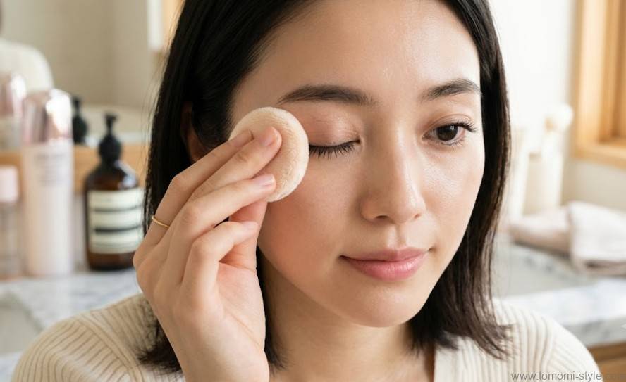 余分な油分を取り除くために柔らかい化粧パウダーパフをまぶたに優しく当てている20代日本人女性の接写実写写真。